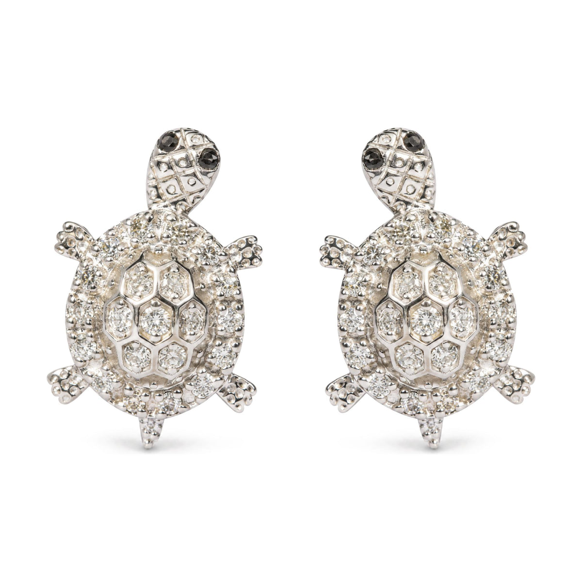 Close-up front view of a pair of white metal turtle-shaped earrings adorned with multiple round white gemstones and small round black gemstones on the turtle heads, shown on a white background.