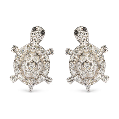 Close-up front view of a pair of white metal turtle-shaped earrings adorned with multiple round white gemstones and small round black gemstones on the turtle heads, shown on a white background.