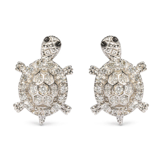 Close-up front view of a pair of white metal turtle-shaped earrings adorned with multiple round white gemstones and small round black gemstones on the turtle heads, shown on a white background.