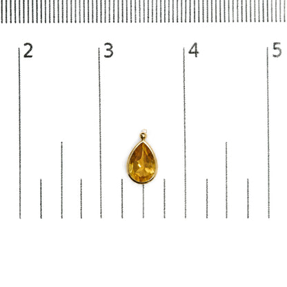 Close-up front view of a single yellow metal earring with a pear-shaped yellow gemstone in bezel setting, shown on a white background with a ruler for scale.