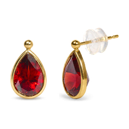 Close-up front angle of yellow metal earrings with pear-shaped red gemstones in bezel settings, shown on a white background.