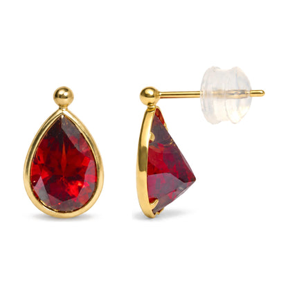 Close-up image showing yellow metal earrings with large pear-shaped red gemstones in bezel settings, displayed from a front and side angle.