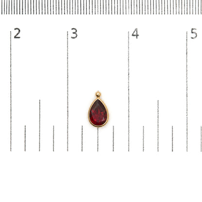 Close-up top-down view of a yellow metal earring featuring a pear-shaped red gemstone in bezel setting, shown on a measurement scale.