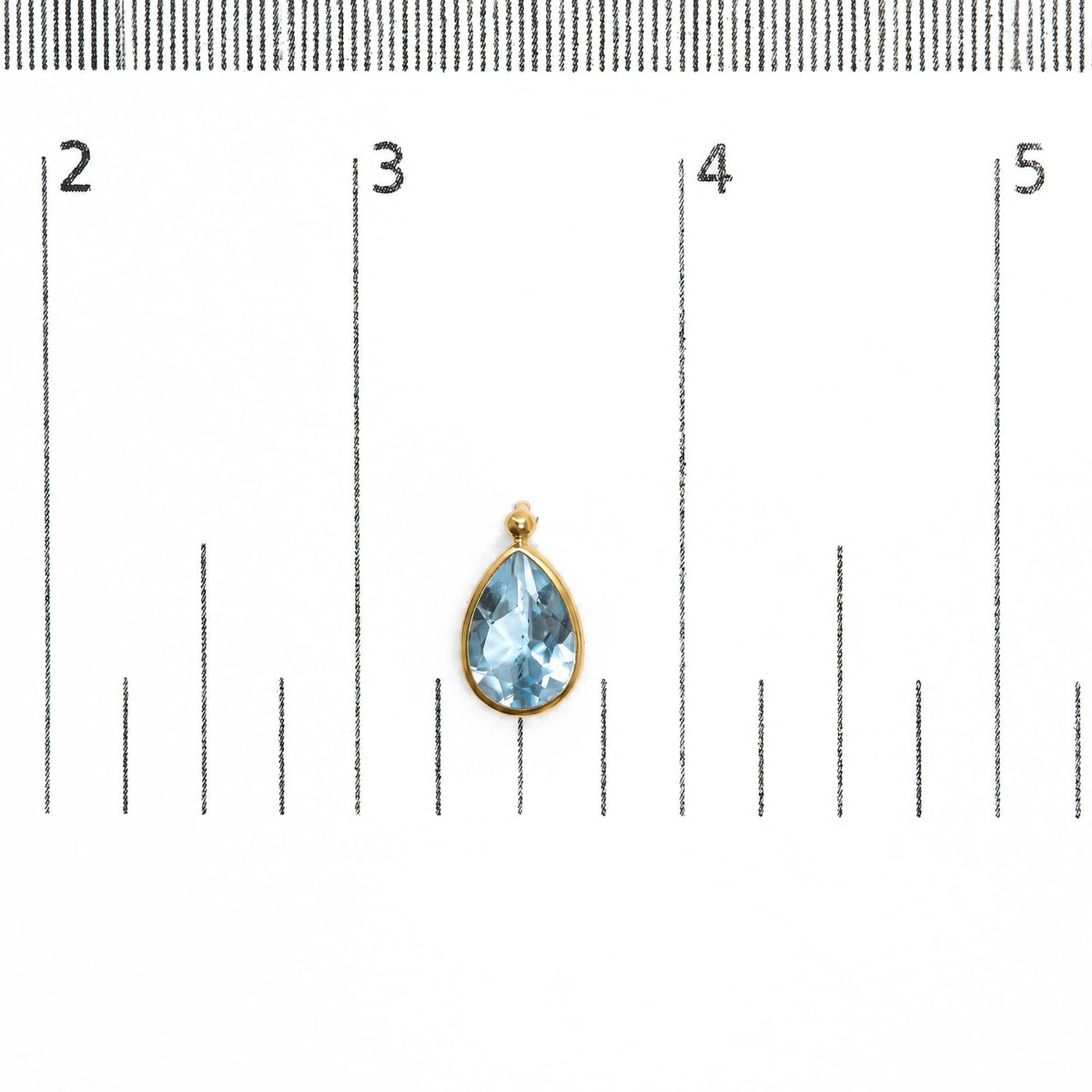 Close-up front view of a yellow metal earring with a pear-shaped blue gemstone in bezel setting, shown on a scale.