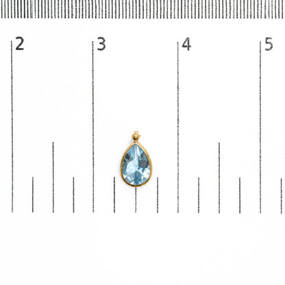 Close-up front view of a yellow metal earring with a pear-shaped blue gemstone in bezel setting, shown on a scale.