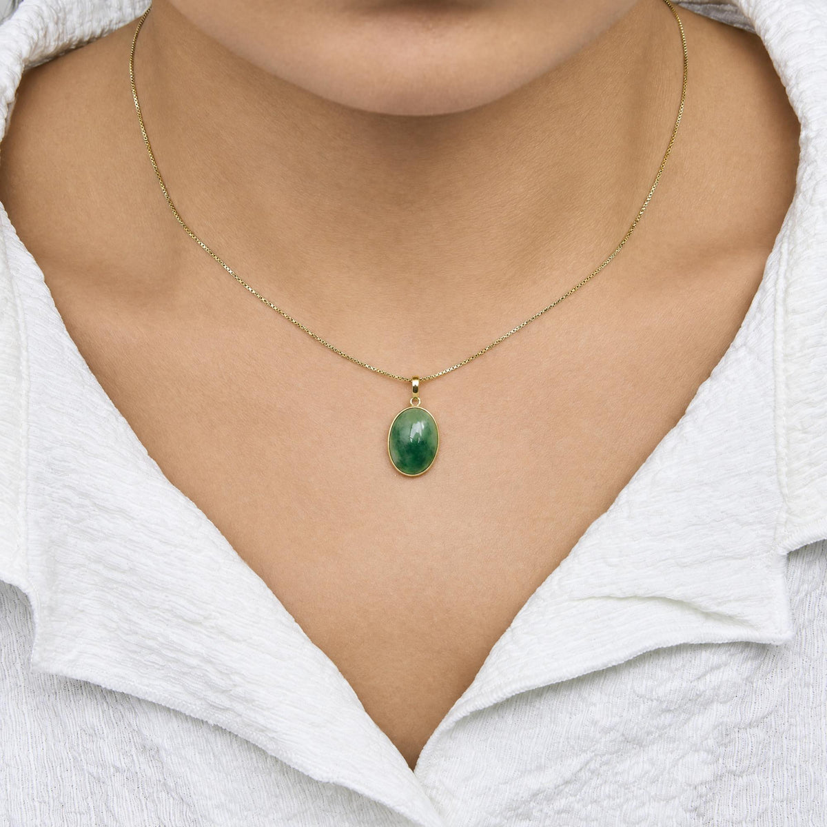 Close-up front view of a model wearing a yellow metal necklace with an oval-shaped green gemstone pendant in bezel setting.