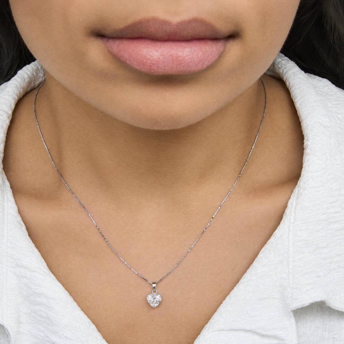Close-up front view of a model wearing a white metal necklace with a heart-shaped white gemstone pendant in a 3-prong setting.