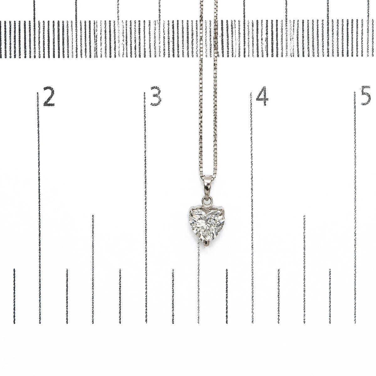 Close-up front view of a white metal necklace with a heart-shaped white gemstone pendant shown on a ruler for scale.
