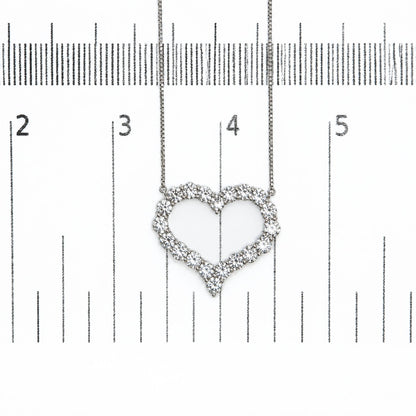 Close-up of a heart-shaped necklace pendant with white round prong-set gemstones, shown on a ruler scale from a top-down angle.