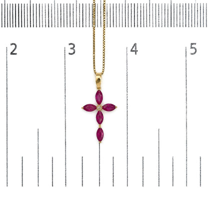 Close-up front view of a yellow metal necklace with a cross-shaped pendant featuring marquise-shaped red gemstones and a round white gemstone in the center, shown on a scale.