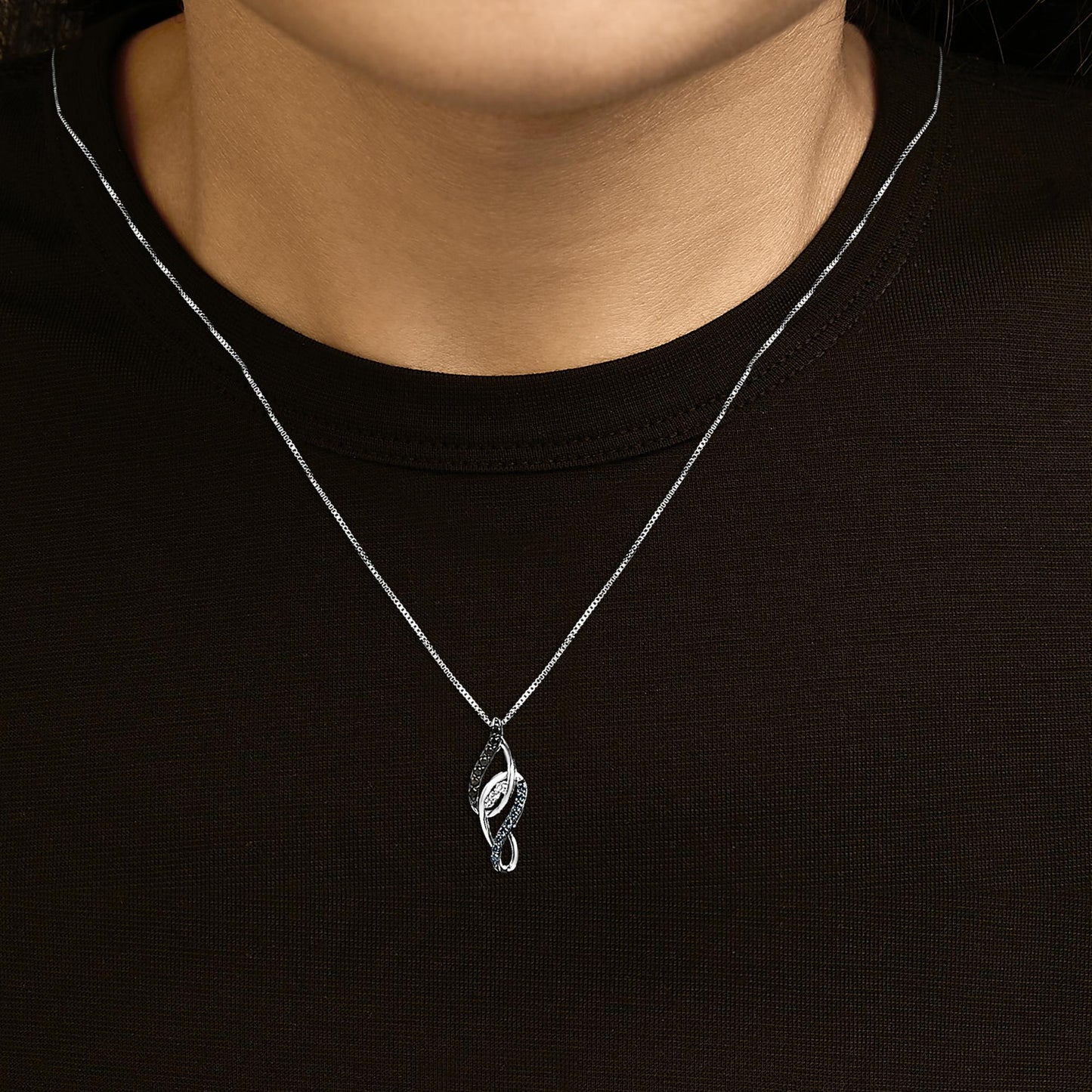 White metal necklace with a pendant shown worn on a model, featuring a curving leaf-shaped design set with round white, blue, and black gemstones, photographed from the front.