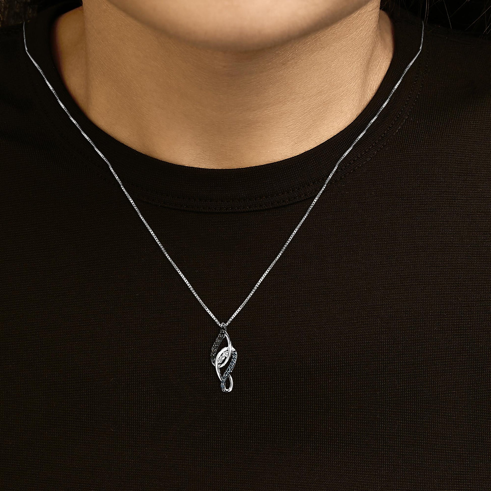 White metal necklace with a pendant shown worn on a model, featuring a curving leaf-shaped design set with round white, blue, and black gemstones, photographed from the front.