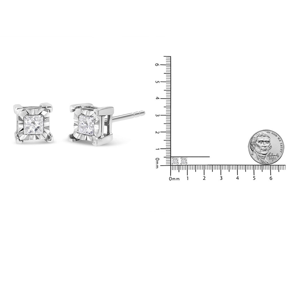 Pair of white metal princess-shaped gemstone stud earrings shown in a side angle with a ruler and a coin for size reference.