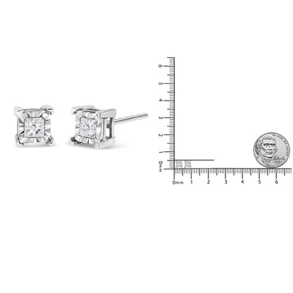 Pair of white metal princess-shaped gemstone stud earrings shown in a side angle with a ruler and a coin for size reference.
