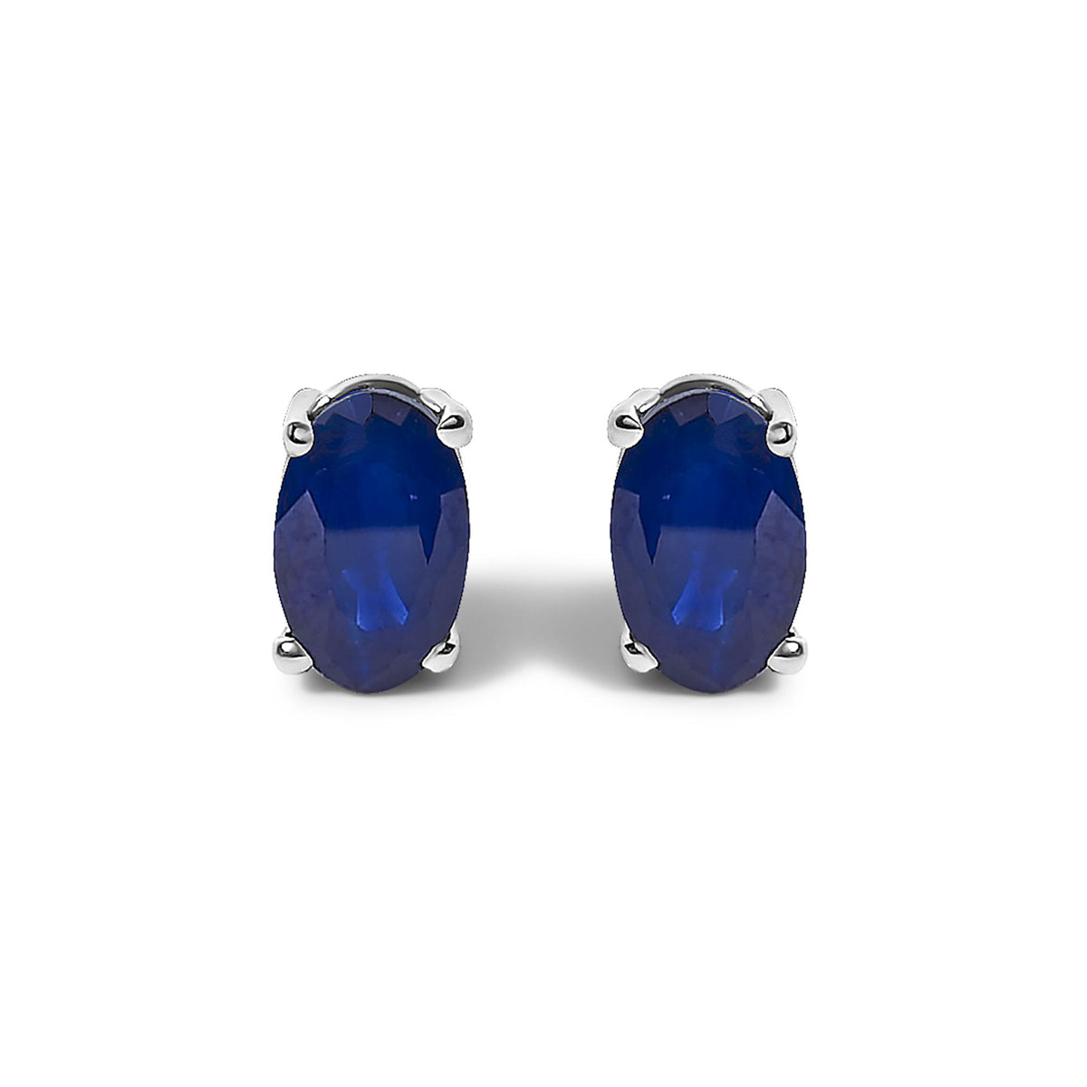 Pair of white metal earrings with oval-shaped blue gemstones in a four-prong setting, shown in a front-facing close-up.