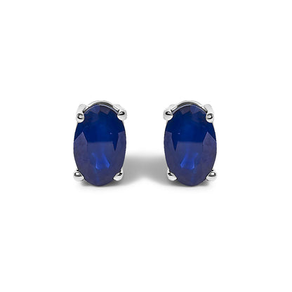 Pair of white metal earrings with oval-shaped blue gemstones in a four-prong setting, shown in a front-facing close-up.