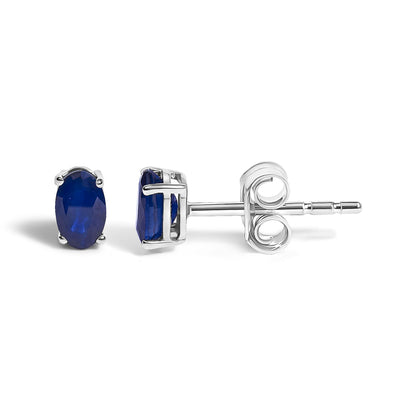 Close-up side and front view of a pair of white metal stud earrings with oval-shaped blue gemstones in four-prong settings on a white background.