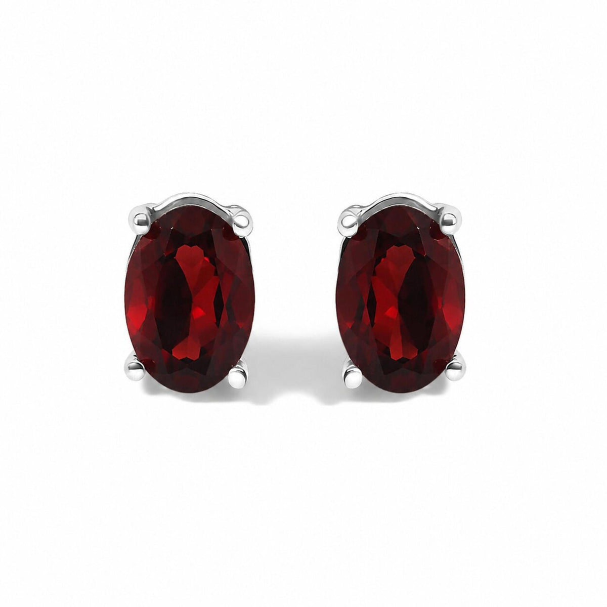 Close-up front view of a pair of white metal earrings each featuring an oval-shaped red gemstone in a four-prong setting, shown on a white background.