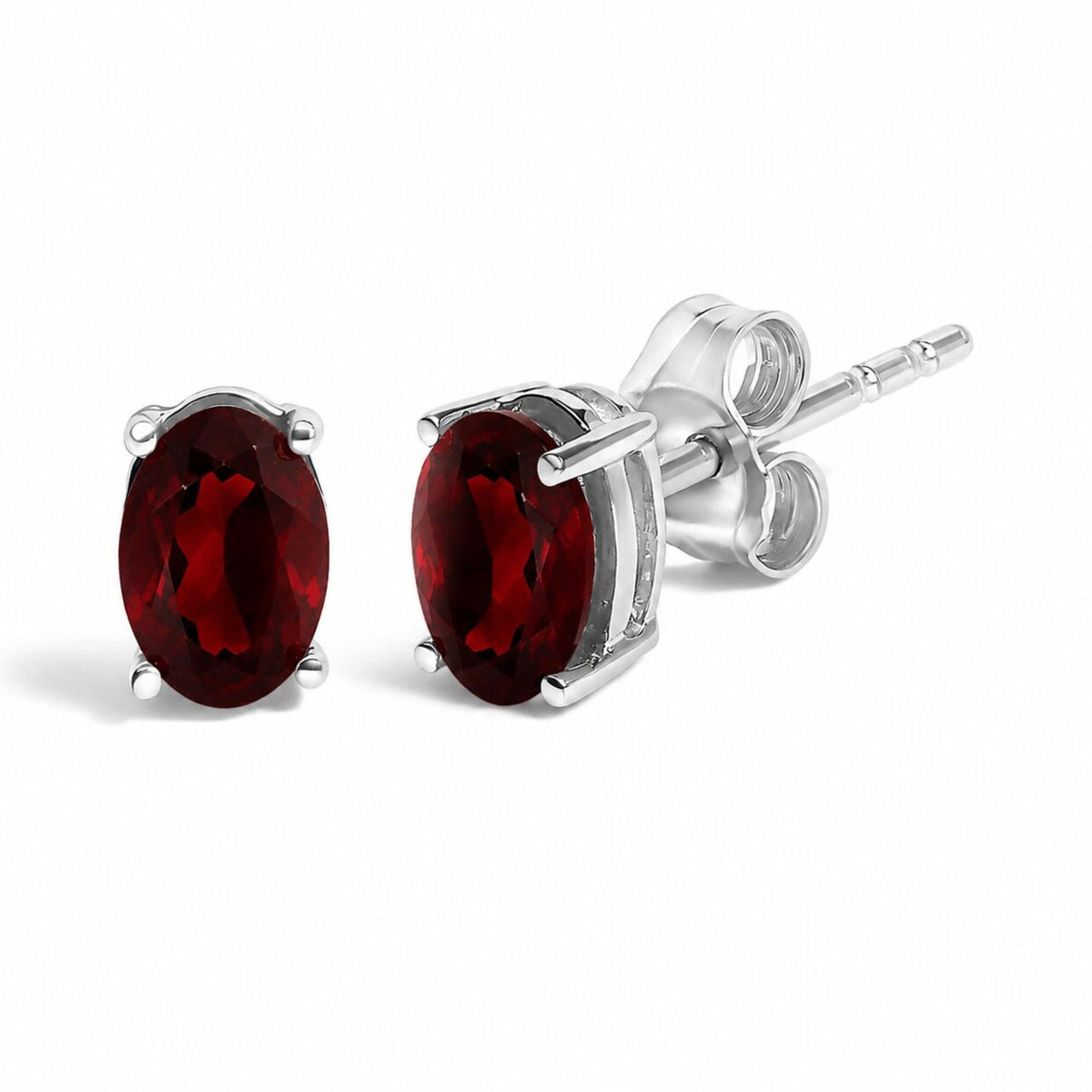 Close-up front and side angle of a pair of white metal stud earrings with oval-shaped red gemstones in a four-prong setting.