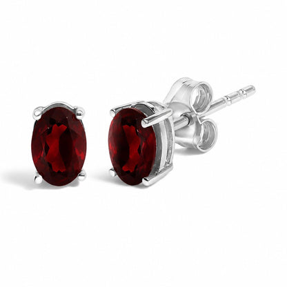 Close-up front and side angle of a pair of white metal stud earrings with oval-shaped red gemstones in a four-prong setting.