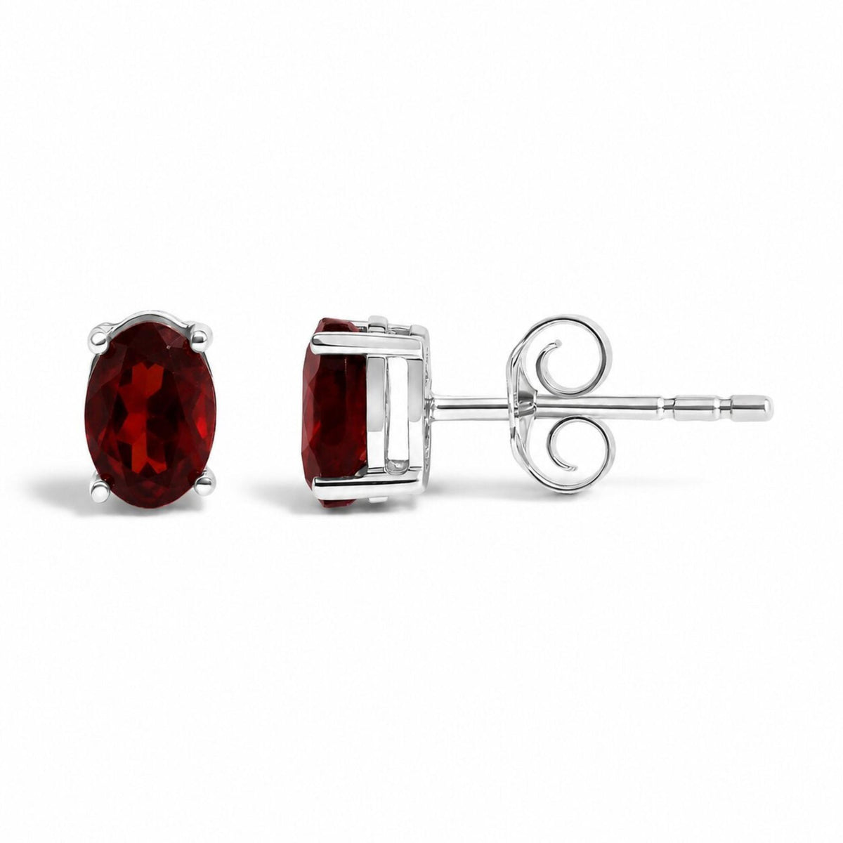 Close-up front and side views of white metal stud earrings with oval-shaped red gemstones in four-prong settings, shown on a white background.