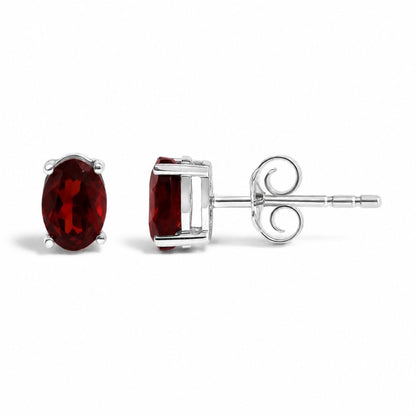 Close-up front and side views of white metal stud earrings with oval-shaped red gemstones in four-prong settings, shown on a white background.