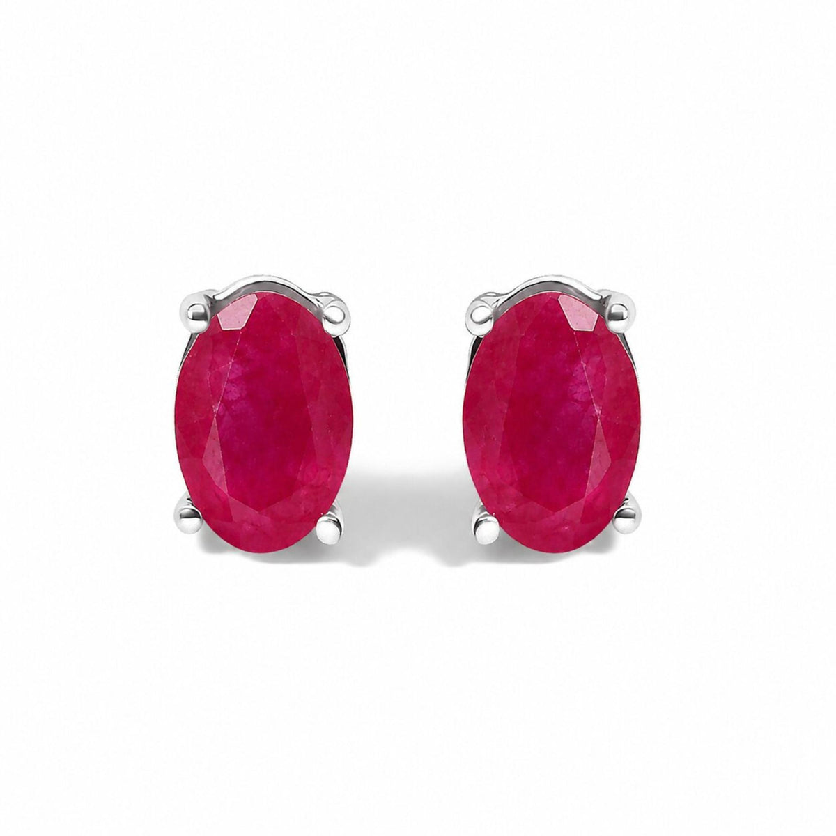 Close-up front angle of a pair of white metal stud earrings featuring oval-shaped red gemstones in four-prong settings shown on a white background.