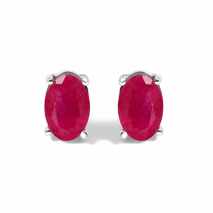Close-up front angle of a pair of white metal stud earrings featuring oval-shaped red gemstones in four-prong settings shown on a white background.