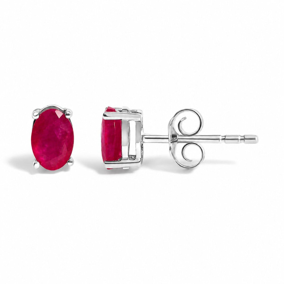 Close-up front and side views of a pair of white metal stud earrings featuring oval-shaped red gemstones in 4-prong settings, shown laid flat on a white surface.