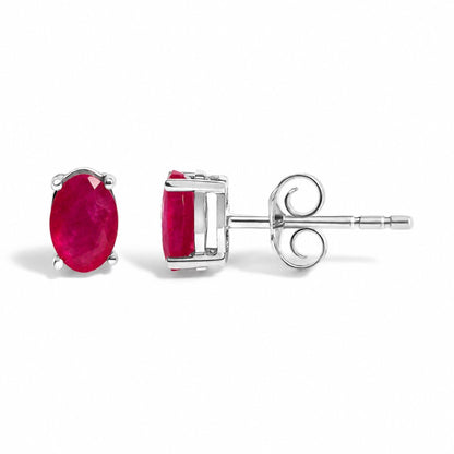 Close-up front and side views of a pair of white metal stud earrings featuring oval-shaped red gemstones in 4-prong settings, shown laid flat on a white surface.