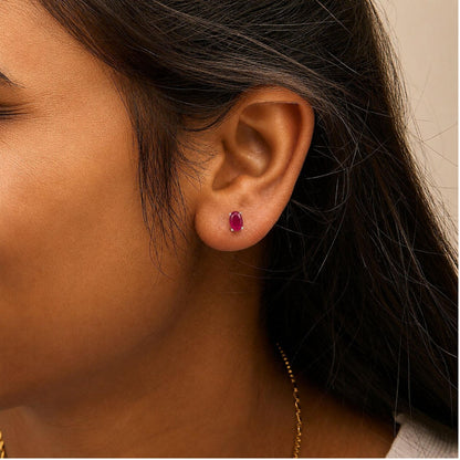 Close-up side view of a model wearing oval-shaped red gemstone stud earrings set in a white metal with a four-prong setting.