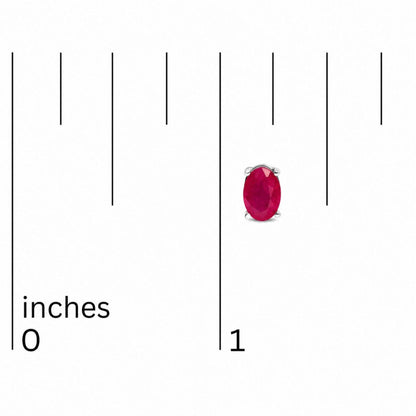 Close-up front view of oval-shaped red gemstone stud earrings in white metal with four-prong settings, shown on a scale.