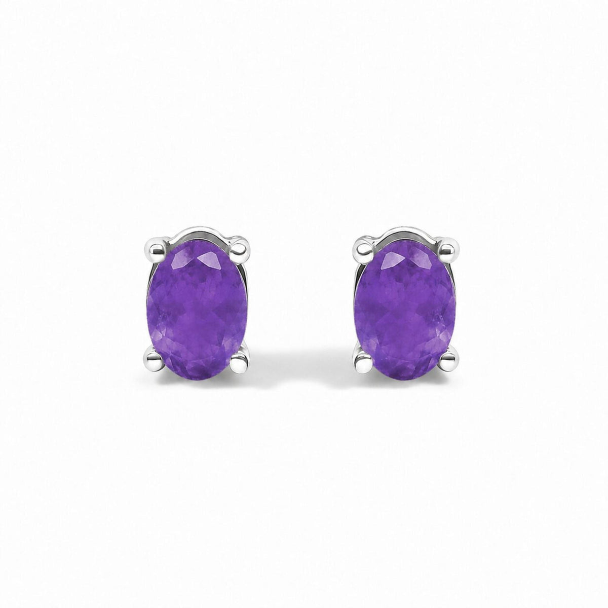 Pair of white metal stud earrings with oval purple gemstones in four-prong settings, shown in a close-up front angle.