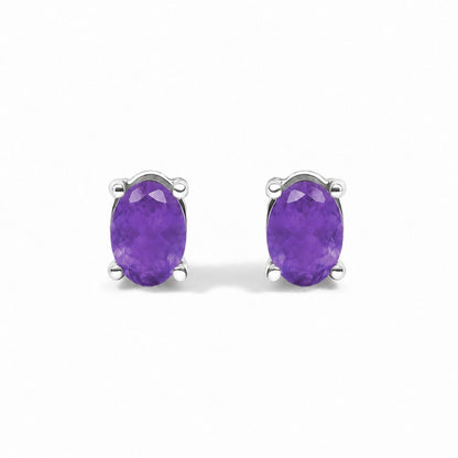 Pair of white metal stud earrings with oval purple gemstones in four-prong settings, shown in a close-up front angle.