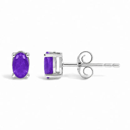 Front and side close-up view of white metal stud earrings featuring an oval purple gemstone set with four prongs, shown on a white background.
