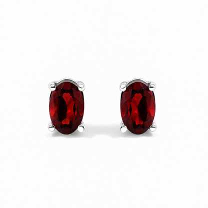 Close-up front view of a pair of white metal stud earrings featuring oval-shaped red gemstones in four-prong settings against a white background.
