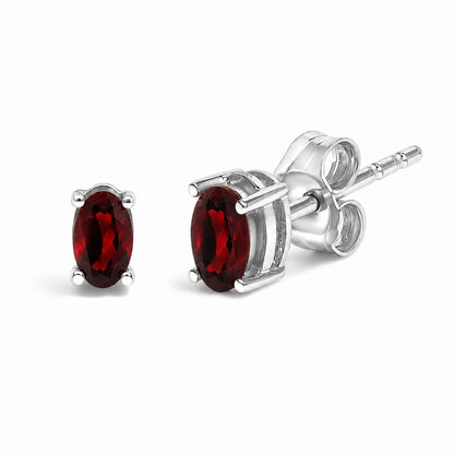 Close-up front and side angle of a pair of white metal stud earrings with oval red gemstones in a four-prong setting.