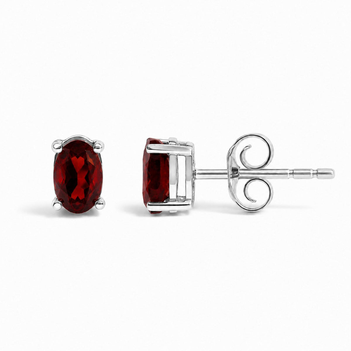 Close-up image of a pair of white metal stud earrings with oval-shaped red gemstones in 4-prong settings, shown from the front and side angles on a white background.