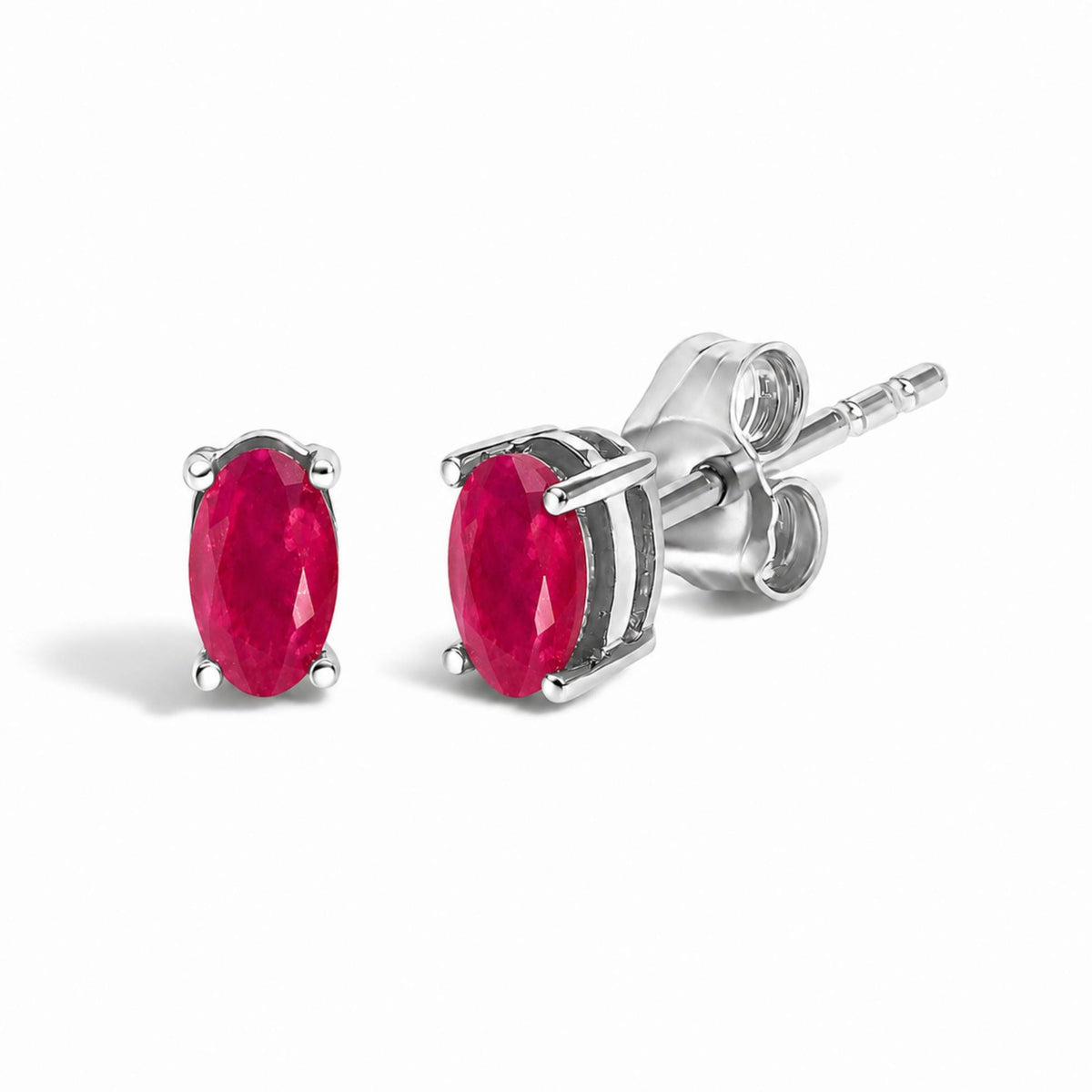 Close-up angled view of a pair of white metal stud earrings each featuring an oval red gemstone in a four-prong setting.