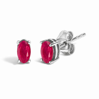 Close-up angled view of a pair of white metal stud earrings each featuring an oval red gemstone in a four-prong setting.