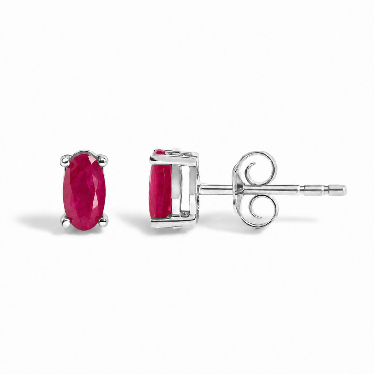 Close-up image of white metal stud earrings with oval red gemstones in four-prong settings, shown from the front and side angles on a white background.