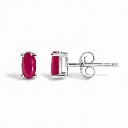 Close-up image of white metal stud earrings with oval red gemstones in four-prong settings, shown from the front and side angles on a white background.