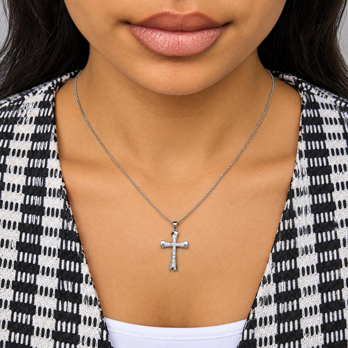 Close-up front view of a model wearing a white necklace with a cross-shaped pendant featuring multiple round white gemstones in prong settings.