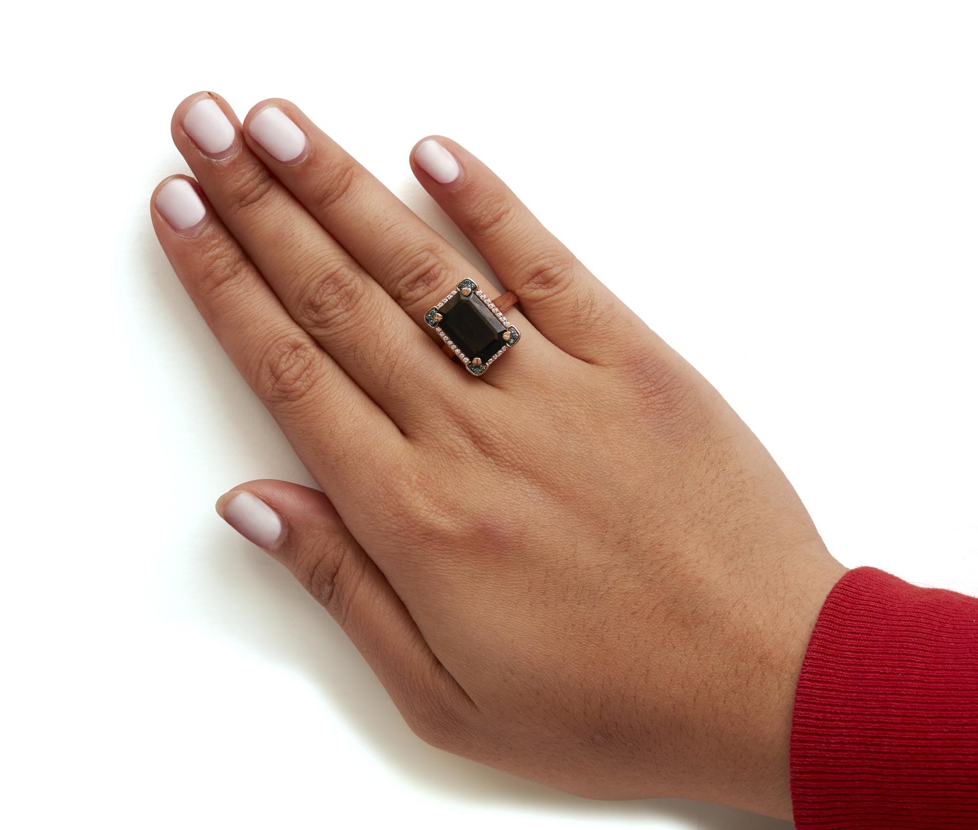 Rose-colored ring with a large black emerald-shaped gemstone in a four-prong setting, surrounded by white and blue round pave-set gemstones, shown worn on a model's hand from a top angle.