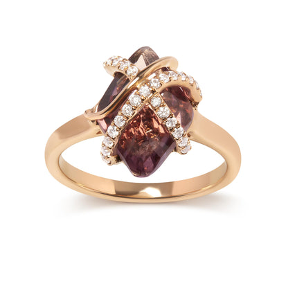 Close-up front angle of a rose metal ring featuring a central marquise-shaped purple gemstone held by tension setting and crossed by two bands set with small round white gemstones in a pave setting.