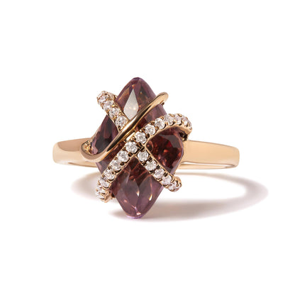 Rose metal ring with a marquise-shaped purple gemstone in a tension setting, crossed by two bands of pave-set round white gemstones, shown in a close-up angled front view.