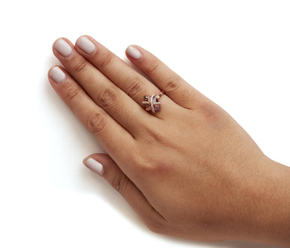 Rose metal ring with a purple marquise gemstone in tension setting and round white gemstones in pave setting, shown worn on a model's hand from a top angle.