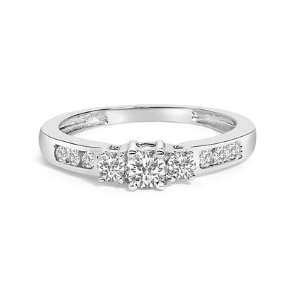 White metal ring with a center round white gemstone in a four-prong setting, flanked by two smaller round white gemstones also in four-prong settings, and additional round white gemstones in channel settings on the band, shown from a front angle on a white background.