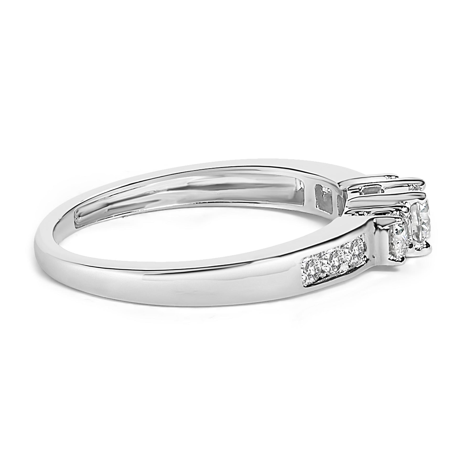 White metal ring with a round white gemstone in a 4-prong setting flanked by two smaller round white gemstones also in 4-prong settings, and multiple round white gemstones in channel settings along the band, shown at a side angle.