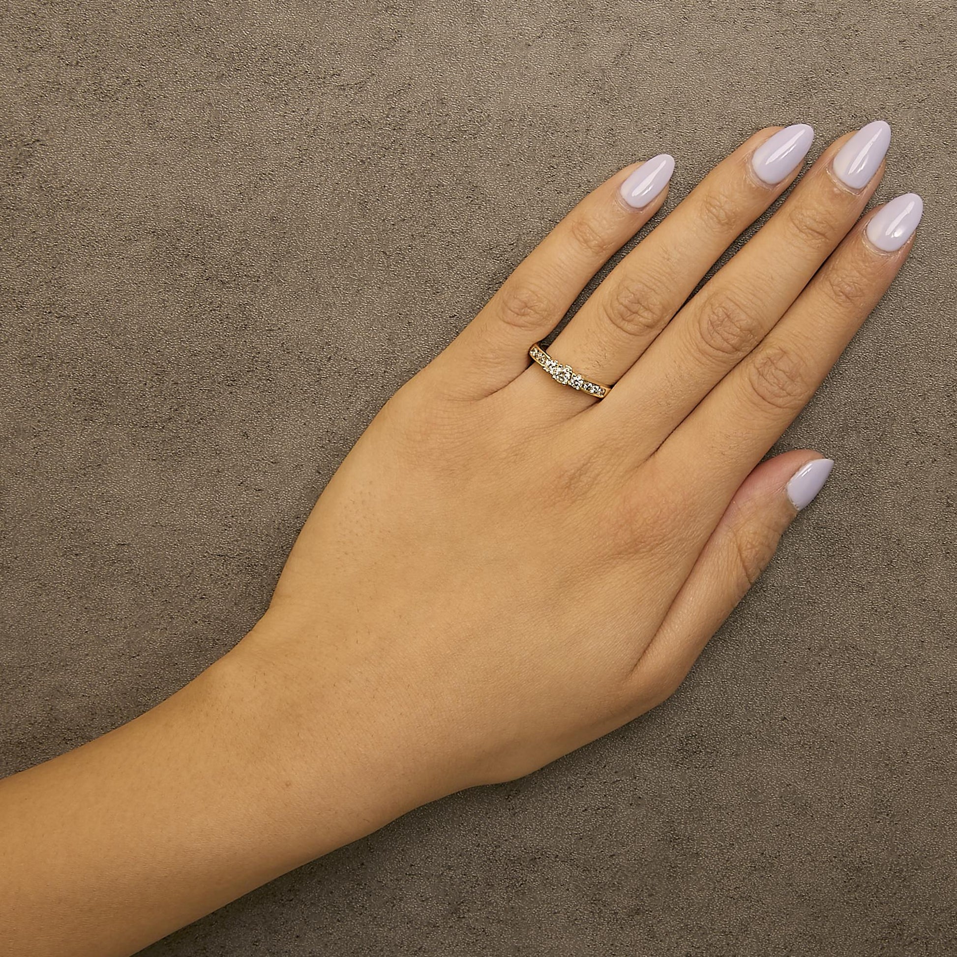 Yellow metal ring with round white gemstones in 4-prong and channel settings, shown worn on a model's hand from a top angle.